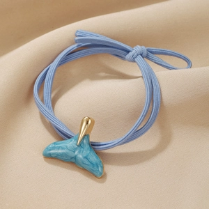 Macro detail of blue elastic hair tie featuring a marble whale tail gold metal pendant