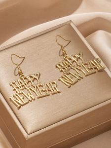 Gros plan détaillé des boucles d'oreilles dorées Happy New Year sur un fond en satin doré