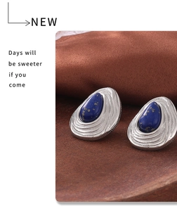 Detailed close-up of retro silver drop earrings with blue stone on silk and wood