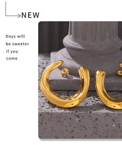 Detailed close-up of chunky gold U-shaped earrings on a stone pedestal with high polish