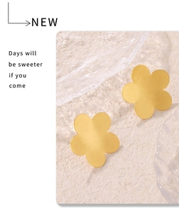 Close-up of matte gold 18k plated five-petal flower stud earrings on cream surface