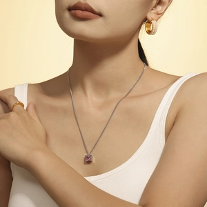 Halskette mit rosa Zirkonia-Anhänger aus Titanstahl an weiblichem Modell mit Perlenohrringen
