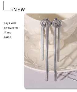 Close-up of silver knotted fringe earrings with sleek snake chains hanging on a cup