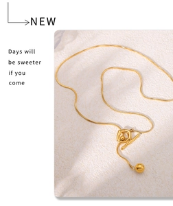 Gros plan d'un collier chaîne serpent dorée avec fermoir OT et pendentif boule sur pierre