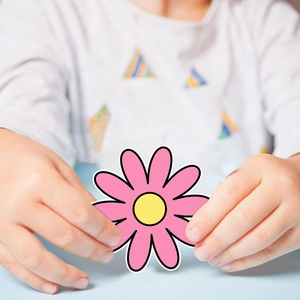 Close-up of a child holding a pink daisy doodle sticker with a bright yellow center