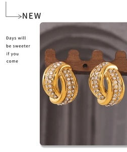 Detail of gold twisted knot earrings with zircon stones hanging on a wooden stand