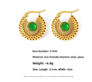 Gros plan de boucles d'oreilles en acier titane doré avec verre vert et motifs ajourés