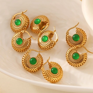 Boucles d'oreilles vintage en or avec verre vert sur un plateau en céramique blanc