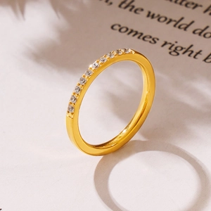 Eleganter goldener Titanring mit CNC-Zirkonsteinen auf weißem strukturiertem Grund