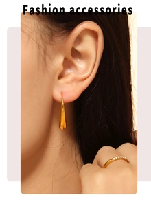 Primer plano de un pendiente de gota dorado minimalista y un anillo brillante en modelo