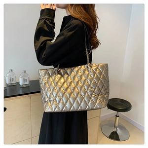 Detail of gold quilted tote bag with diamond stitching and black chain handles