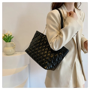 Detail of a large black quilted tote bag with diamond stitching shown on a model