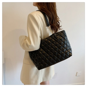 Detail of a large black quilted tote bag with chain strap worn by a model in a beige blazer