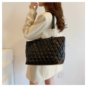 Detail of black quilted tote bag with golden chain strap on shoulder of a model in suit