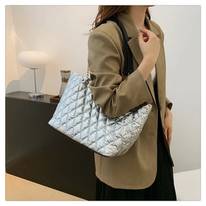 Silver quilted tote bag with black straps in a minimalist indoor setting shot