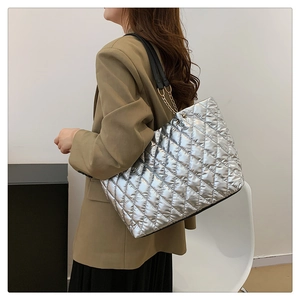 Side view of silver quilted tote bag with gold chain strap on model in professional suit