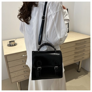 Chic black glossy leather bag worn as a shoulder bag on a white shirt and skirt