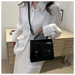Detail of a black glossy retro satchel with double buckle closure and adjustable strap
