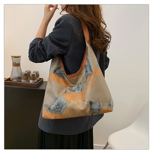 Detail view of large patchwork tote bag in brown leather and blue fabric worn on shoulder