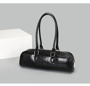 Detail of glossy black cylindrical baguette bag featuring smooth texture and silver hardware