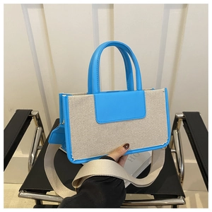 Detail of blue leather trim and wide beige woven shoulder strap on a canvas tote bag