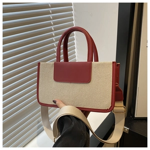 Detail of square tote bag featuring red leather and beige canvas with a wide strap