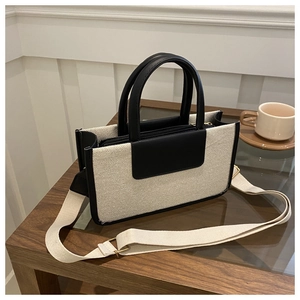 Close-up of canvas and black leather tote bag with wide strap on minimalist wooden table