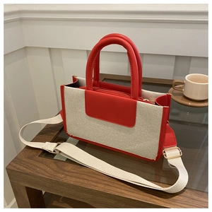 Detail view of woven canvas tote bag with red faux leather trim and golden hardware