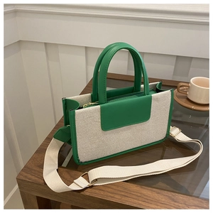 Detail of canvas and green leather tote bag with wide strap on a wooden surface