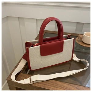 Detail view of a red leather and cream canvas tote bag with adjustable woven shoulder strap