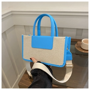 Detailed shot of beige canvas and blue leather tote bag with a wide fabric shoulder strap