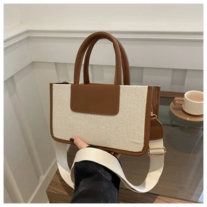 Detail of canvas tote bag with brown leather trim and wide woven shoulder strap