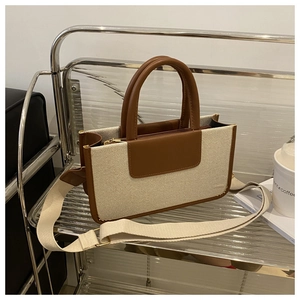 Close-up of canvas and leather tote with wide fabric strap on a metal shelf
