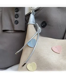 Close-up of beige handbag with colorful leather heart patches and metal knot details