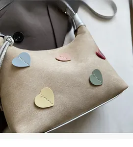 Detail of trendy beige tote bag featuring colorful leather heart patches and stitching