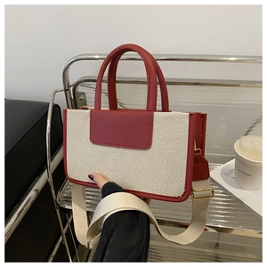 Detail of red leather trim and beige canvas tote bag with a wide fabric shoulder strap