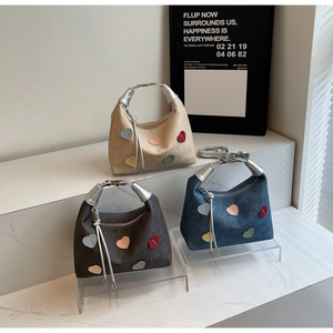 Three crescent handbags with colorful heart patches and silver tassel charms on stands