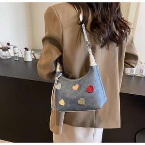 Detail of blue denim hobo bag featuring colorful stitched heart patches and silver hardware