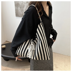 Detailed side view of a black and white striped canvas tote bag with a lace bow accent