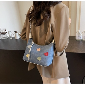 Detail of blue denim shoulder bag with colorful heart patches and silver hardware