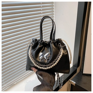 Détail du sac seau plissé noir avec papillon métallique et chaîne de perles élégante