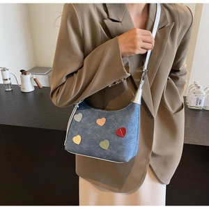 Close-up of denim shoulder bag featuring multi-colored heart patches and blue leather strap