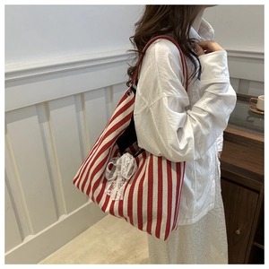 Detailed view of striped canvas tote bag featuring a decorative white lace bow accent