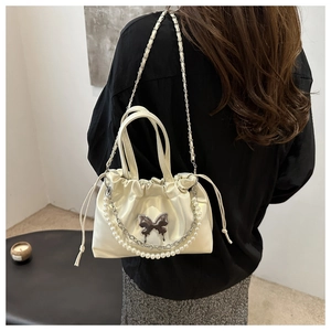 Détail du sac en satin crème avec décoration papillon, chaînes de perles et plis coulissants