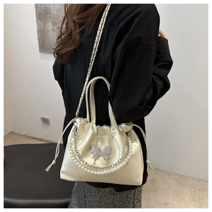 Détail du sac plissé en satin crème avec chaînes de perles et breloque papillon argentée