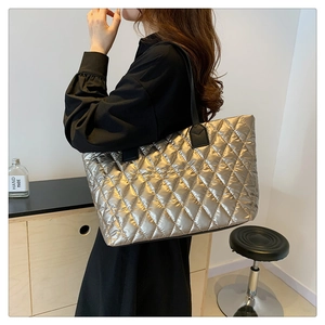 Detail of silver quilted tote bag showing metallic texture and black shoulder straps on model