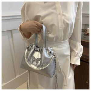 Sac seau argenté avec cordon de serrage, détail papillon et chaîne en perles sur modèle