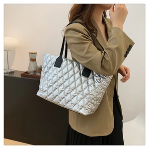 Detail of silver metallic quilted tote bag with diamond lattice pattern and black straps