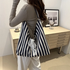 Large striped canvas tote bag with side lace bow detail shown on shoulder in home setting