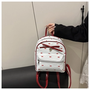 Dettaglio mini zaino bianco con stampa a fiocchi rossi e ciondolo a cuore oro